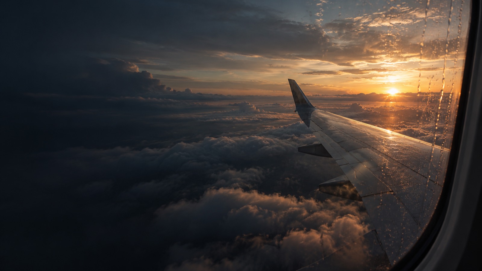 The view from an aircraft window over the wing, above cloud at sunrise
